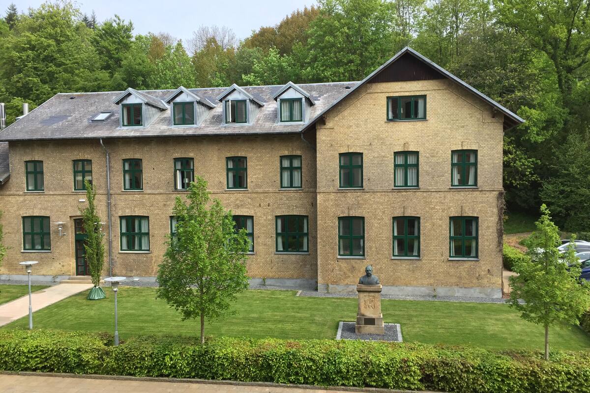A multi-story building with a brick facade, multiple windows, and a small statue in the front garden.