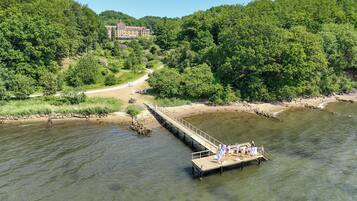 A riverside hotel with a wooden pier extending into the water, surrounded by lush greenery and a clear sky.