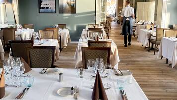 A restaurant with multiple tables set for dining, a waiter walking through, and a chandelier.