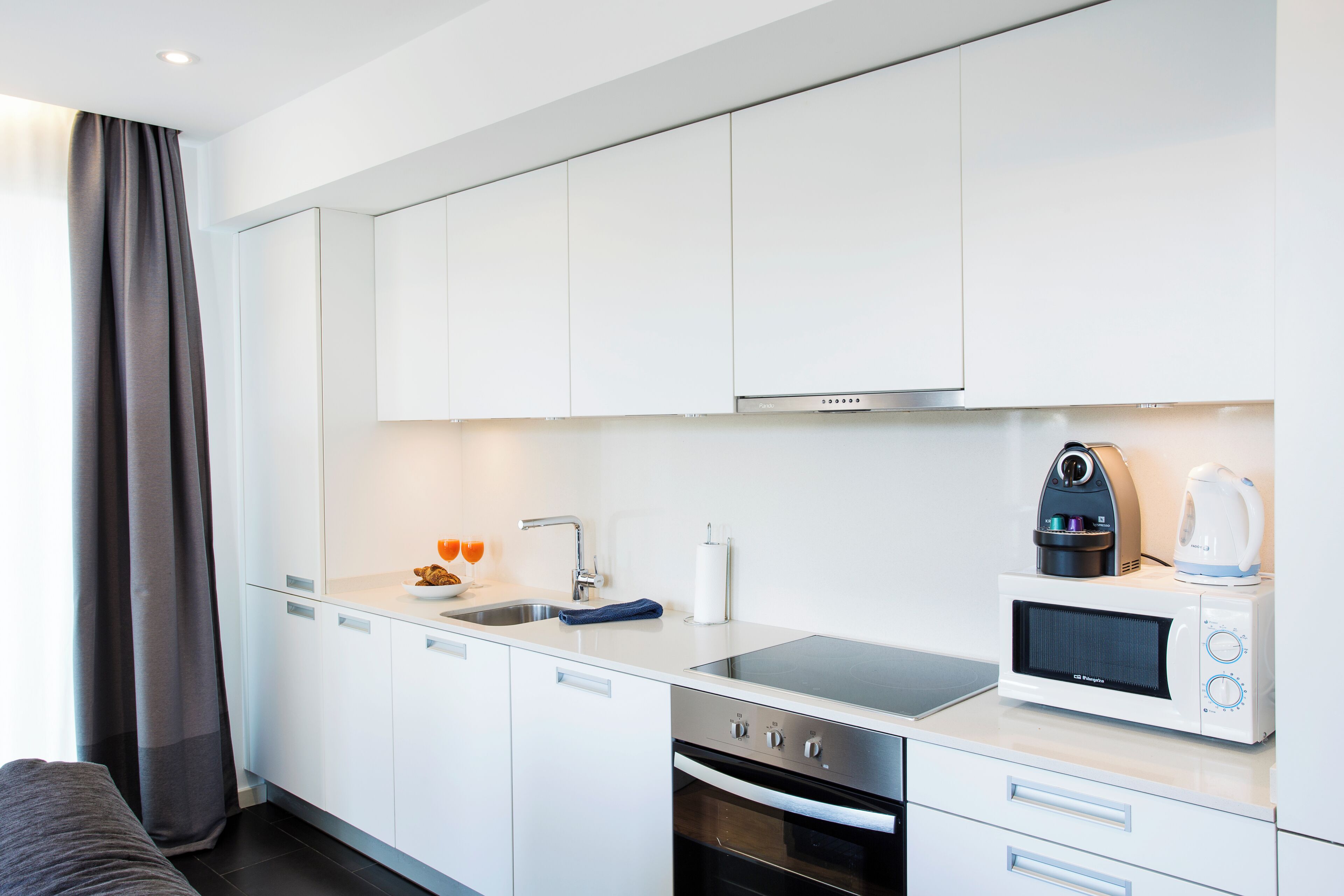 Una cocina moderna con armarios blancos, una campana extractora de acero inoxidable, un microondas empotrado y un hervidor.