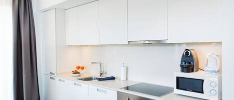 Una cocina moderna con armarios blancos, una campana extractora de acero inoxidable, un microondas empotrado y un hervidor.