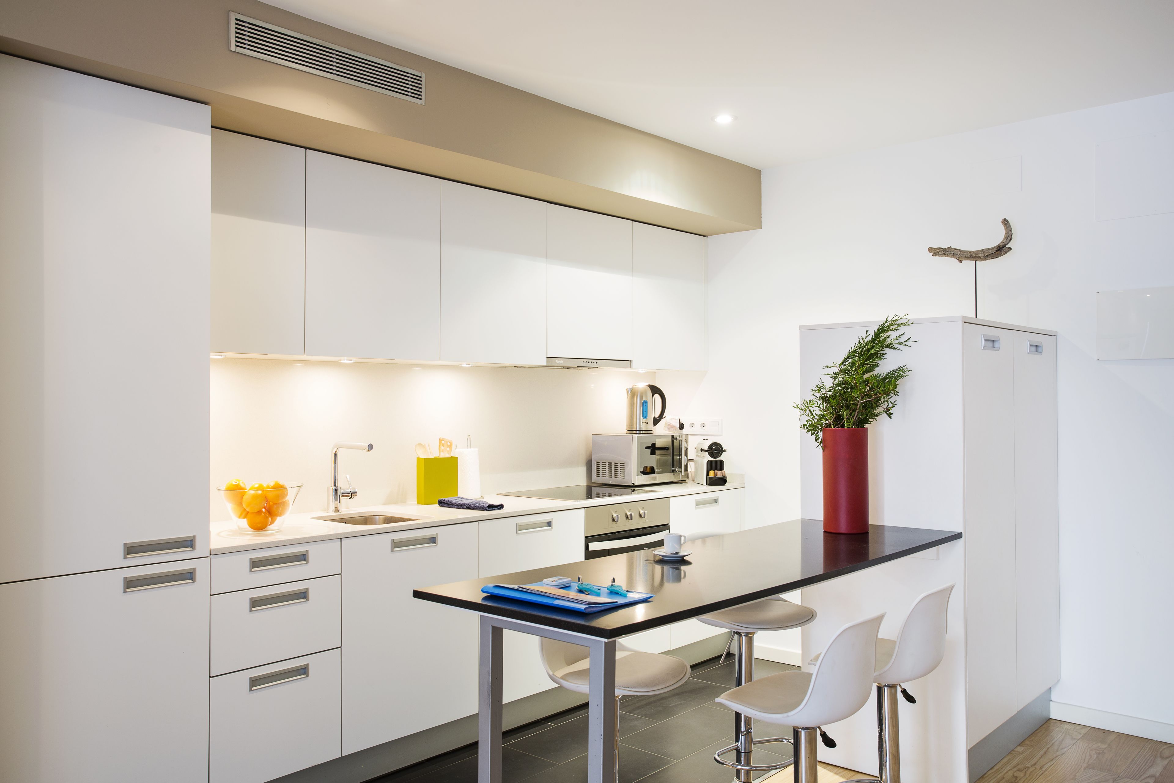 Cocina moderna con armarios blancos, encimera negra y una isla central con taburetes de bar.