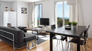 Ein modernes Wohnzimmer mit Sofa, Couchtisch, Fernseher und einem Essbereich mit Stühlen und Tisch.