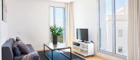 Una sala de estar moderna con un sofá, una mesa de centro, un televisor y un gran ventanal corredizo.