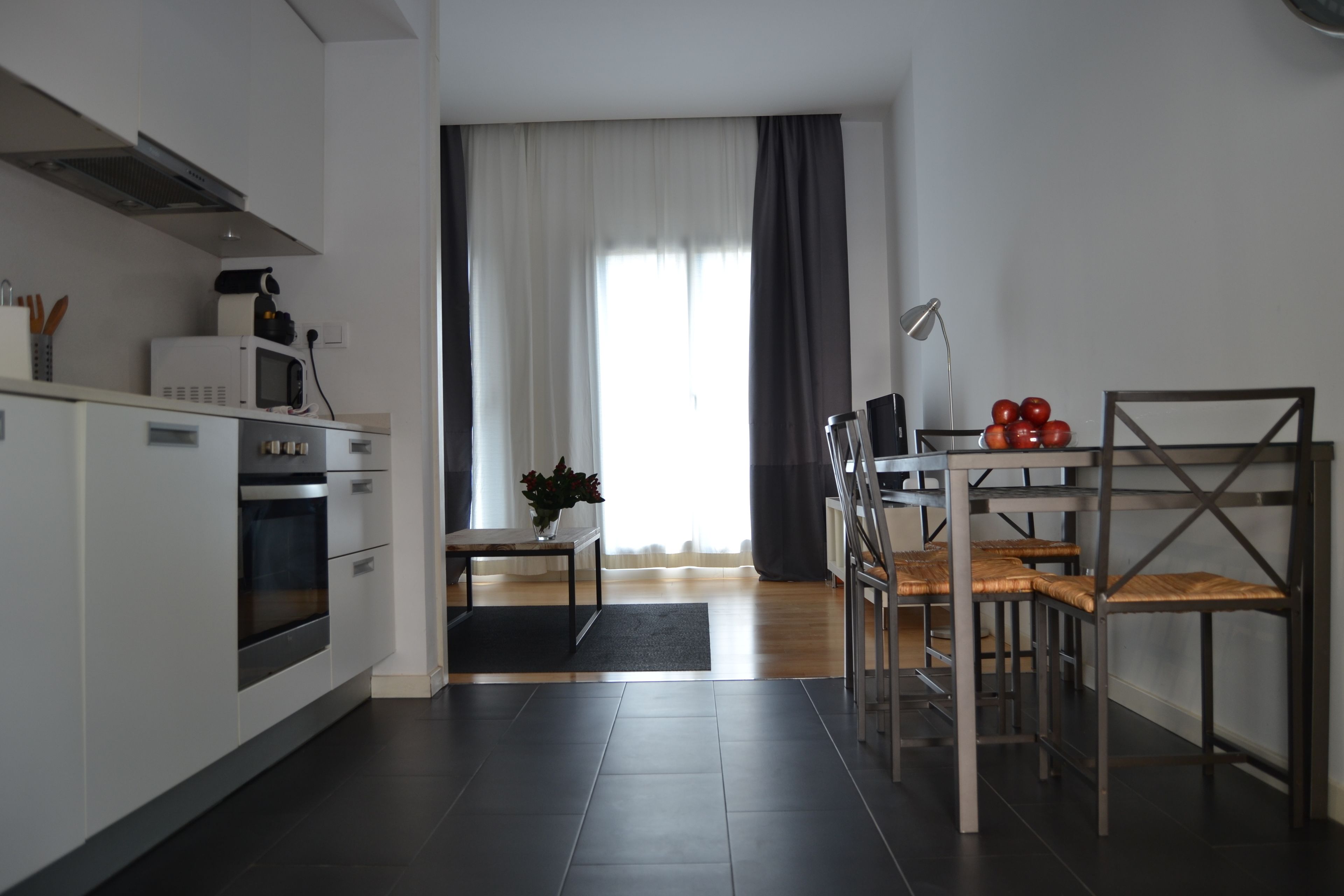 A modern kitchen with white cabinets, a microwave, and a dining area with a table and chairs.