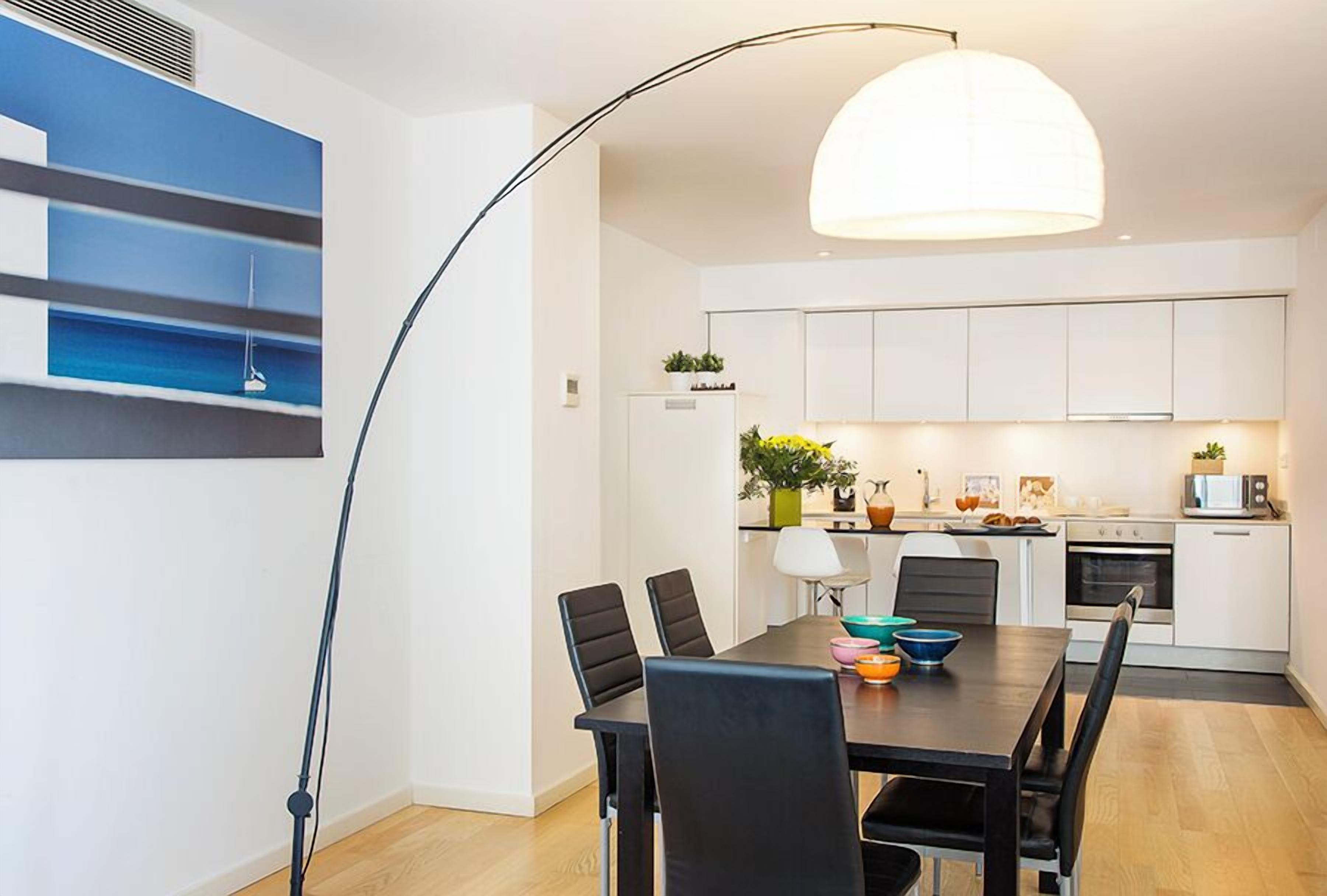 Une cuisine moderne avec des meubles blancs, une table à manger avec des chaises noires et un luminaire suspendu.