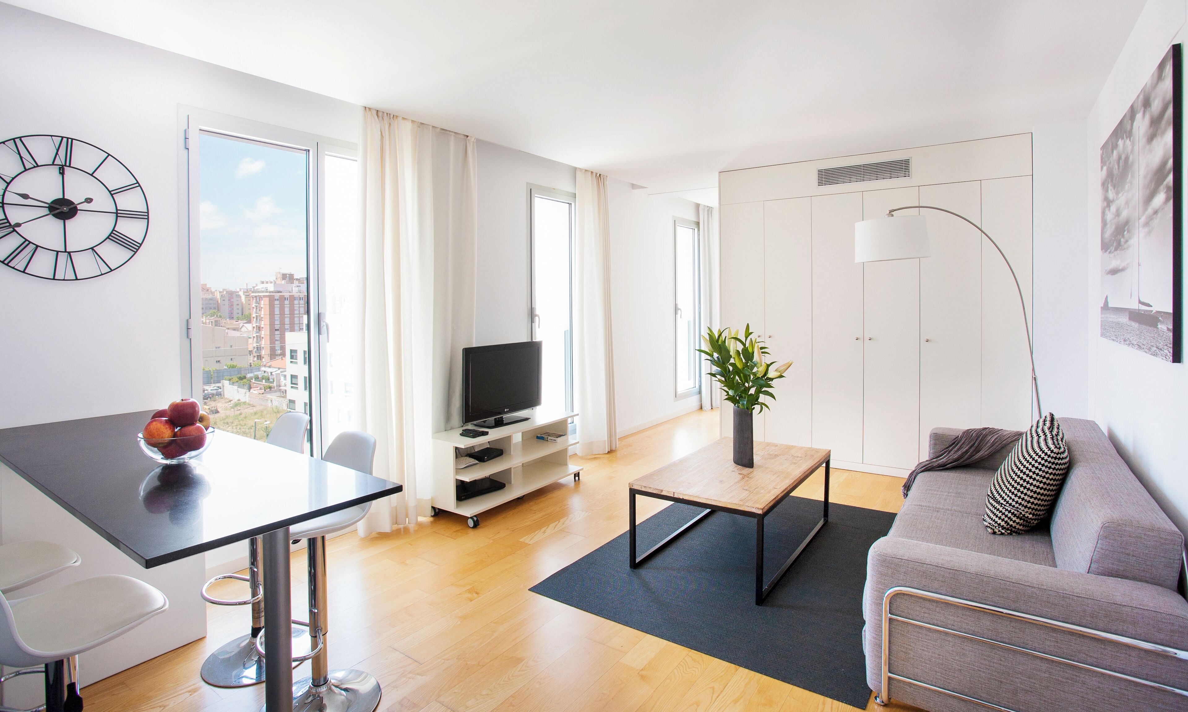 A modern living room with a large window, a flat-screen TV, a dining table, and a sofa.