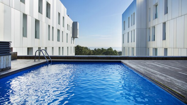 Ein modernes Gebäude mit Swimmingpool, großen Fenstern und blauem Himmel.