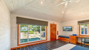 A room with a large sliding glass door to a pool, a wooden desk, a bench, and a television. - Barefoot Cay Resort (Roatan)