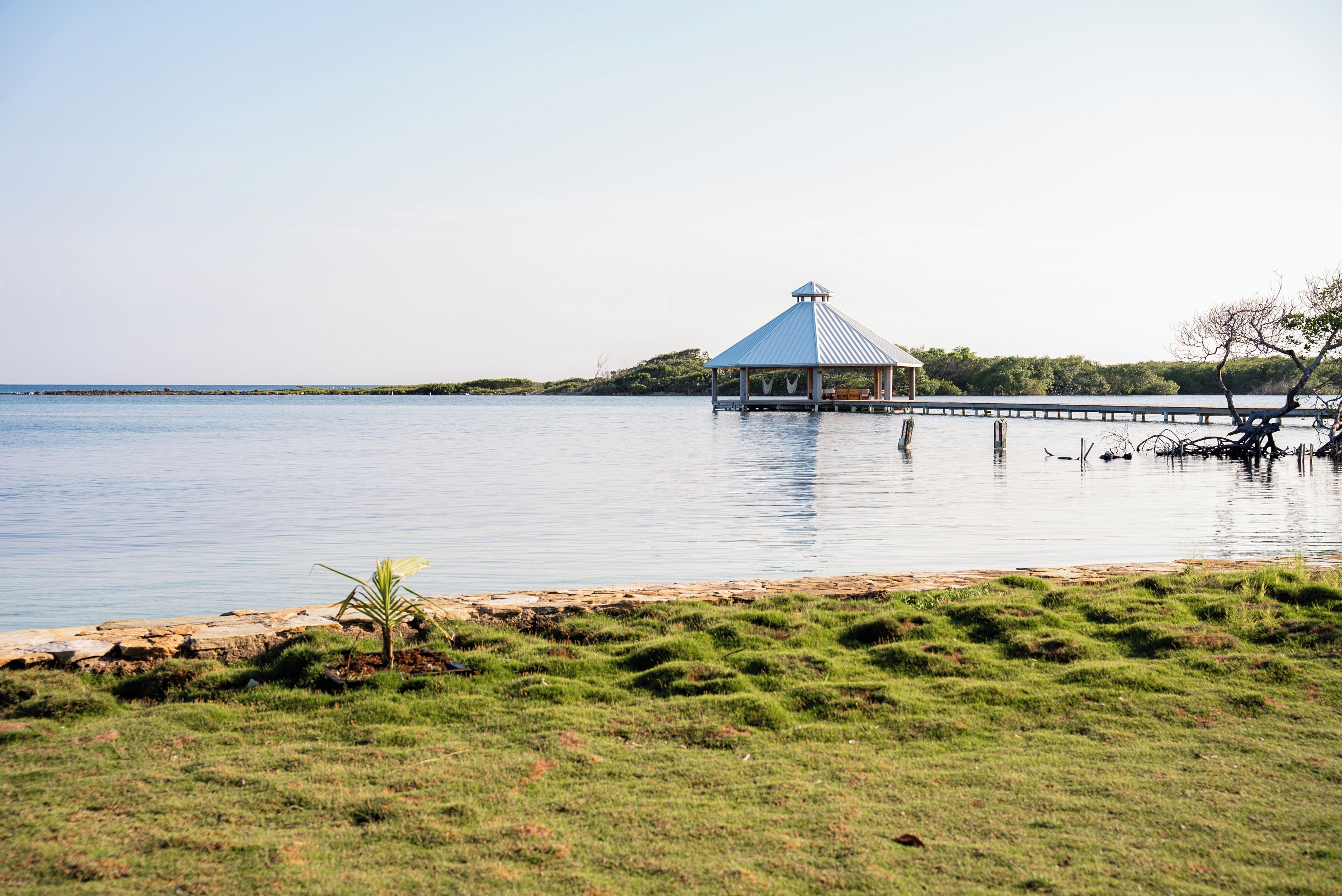 A gazebo on stilts over water, surrounded by grassy areas and trees.