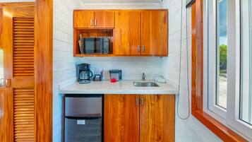 Cocina compacta con armarios de madera, microondas, cafetera y refrigerador.