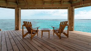 A wooden deck with two wooden chairs and a small table, overlooking turquoise water under a wooden roof. - Barefoot Cay Resort (Roatan)