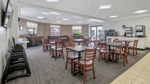 A spacious dining area with multiple tables and chairs, a kitchen area with appliances, and a large window providing natural light.