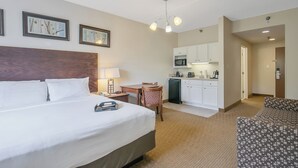 A hotel room with a large bed, a desk, a chair, a microwave, and a kitchenette.