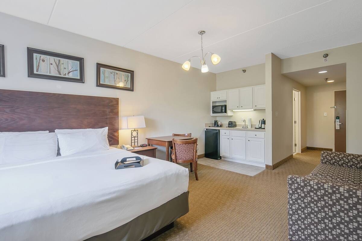A hotel room with a large bed, a desk, a chair, a microwave, and a kitchenette.