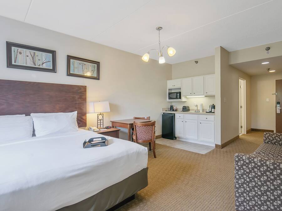 A hotel room with a large bed, a desk, a chair, a microwave, and a kitchenette.