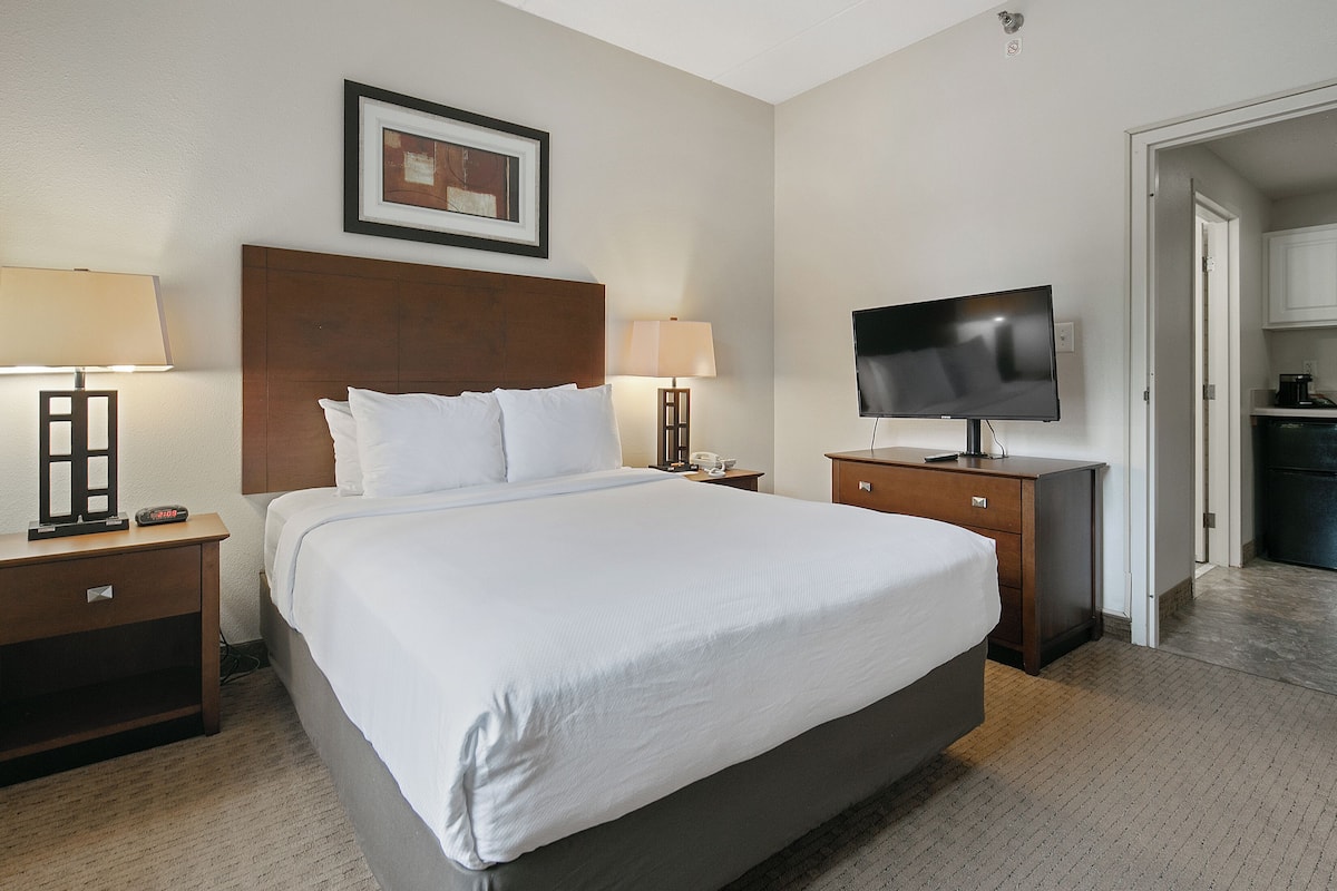 A hotel room with a large bed, two bedside tables with lamps, a flat-screen TV, and a framed picture on the wall.