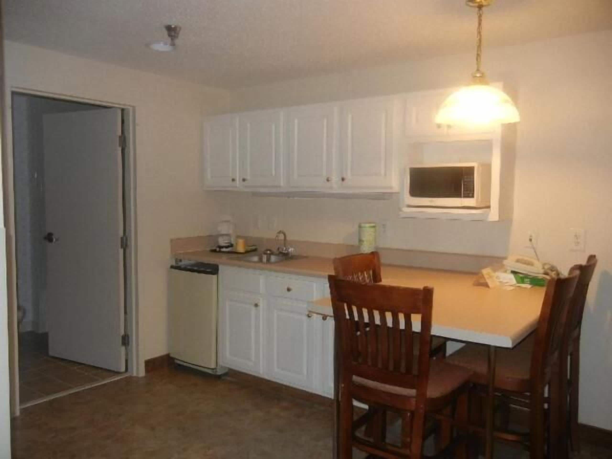 A compact kitchen with white cabinets, a microwave, a sink, and a dining area with two wooden chairs.