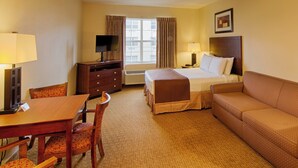 A hotel room with a bed, a sofa, a desk with a chair, a television, and a window with curtains.