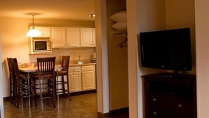 A compact kitchen with white cabinets, a dining table with chairs, a microwave, and a television on a stand.