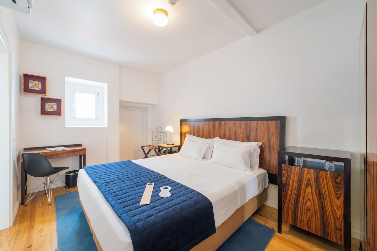 Un dormitorio con cama, escritorio, silla, mesita y armario.