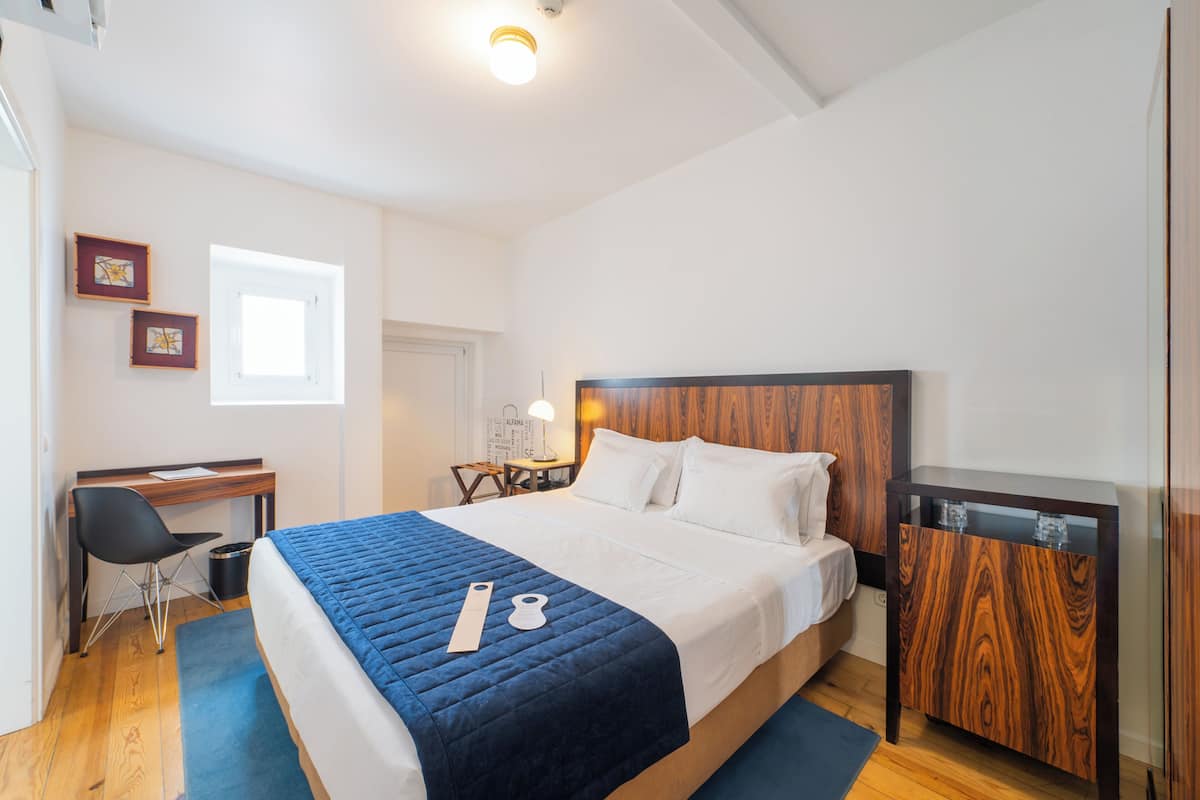 A bedroom with a bed, a desk, a chair, a small table, and a cabinet.