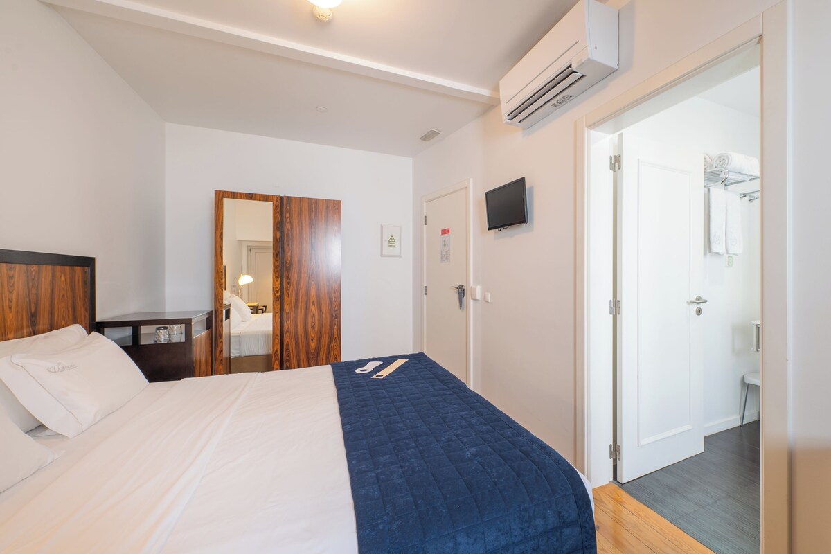 Ein Hotelzimmer mit Bett, einem Holzschrank, einem an der Wand montierten Fernseher und einer Tür zu einem Badezimmer.