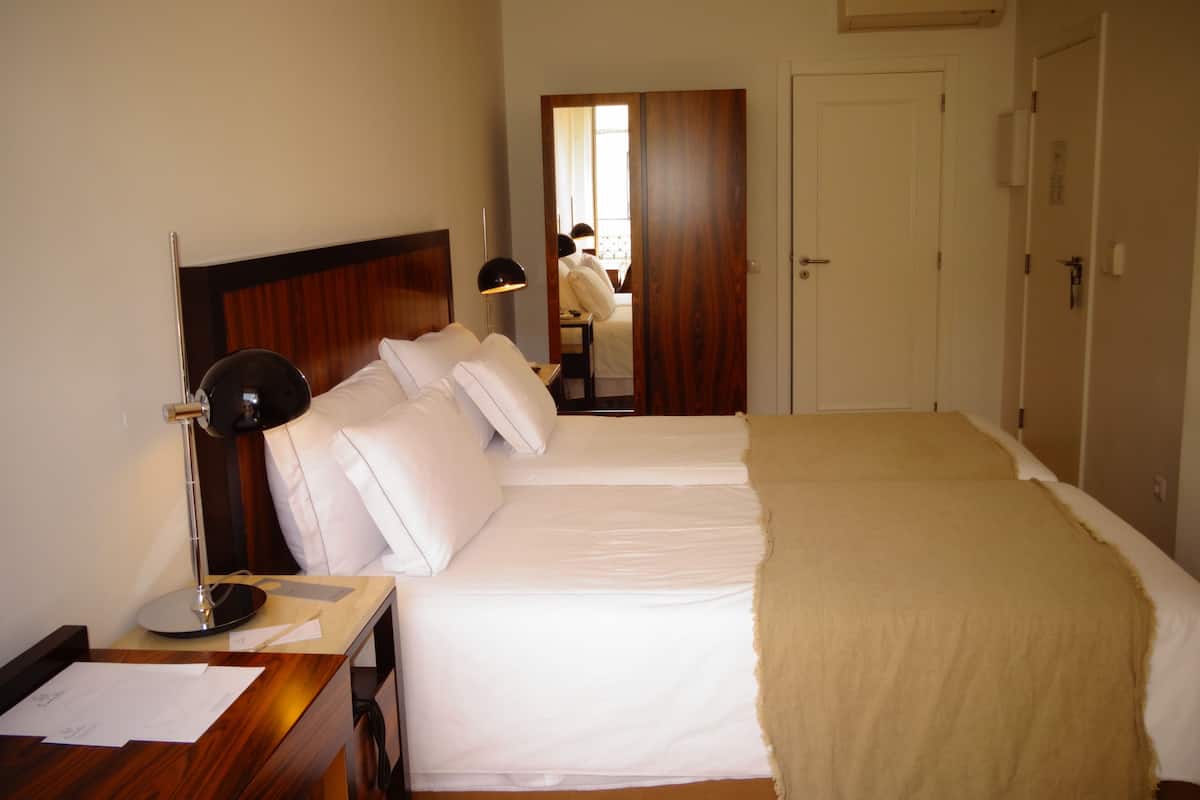 A hotel room with two beds, a desk with papers, a lamp, and a wardrobe.