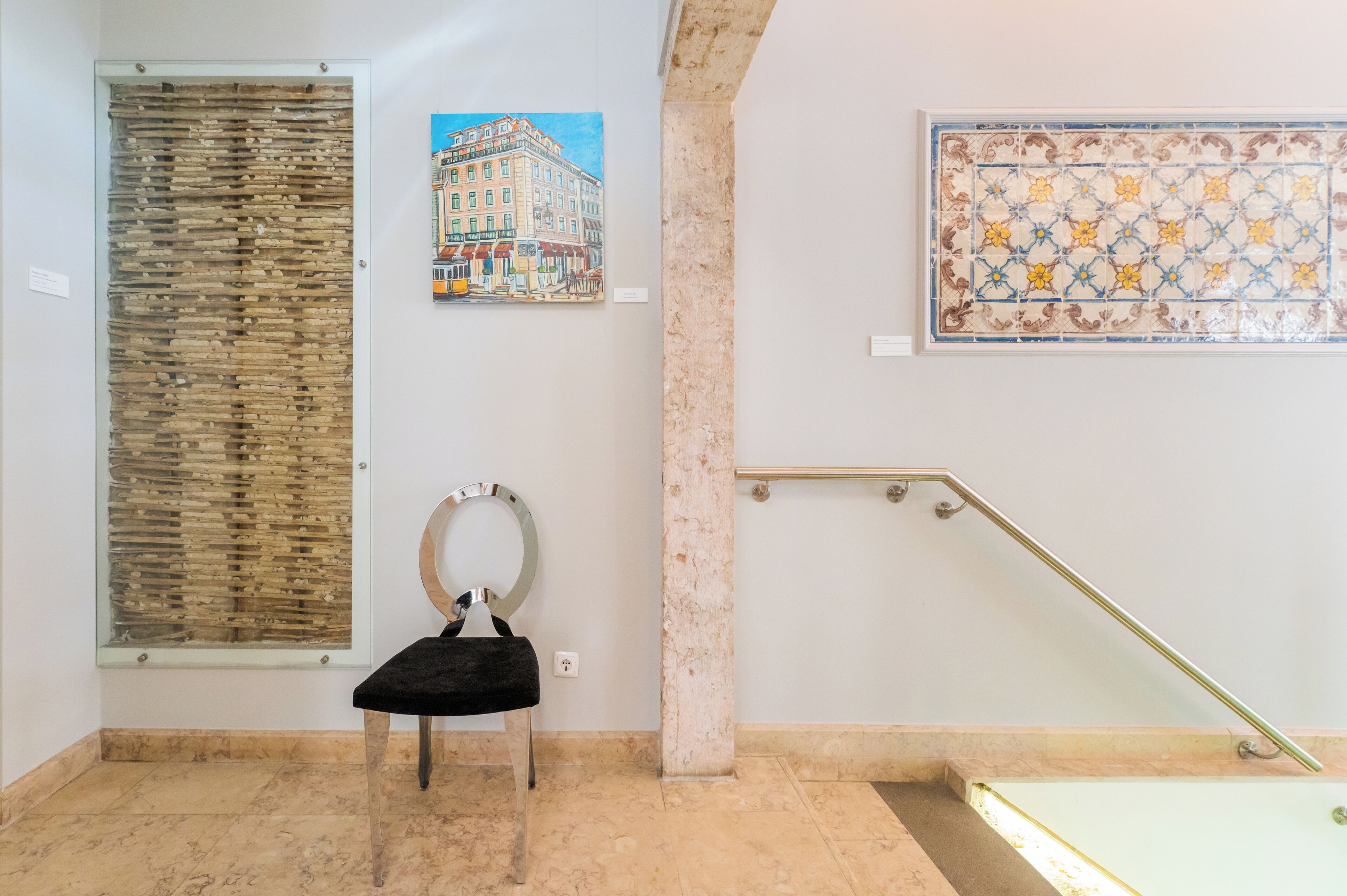 Una habitación con suelo de mármol, una silla negra, un separador de vidrio, un cuadro de un edificio y una pared con azulejos.