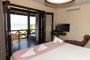 A hotel room with a bed, a TV, a massage chair, and a balcony with a view of the ocean. - Hospedaria Refúgio das Galés (Bombinhas)