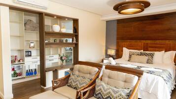 A hotel room with a bed, two wicker chairs, a wooden headboard, a built-in shelf unit, and a ceiling light fixture.
