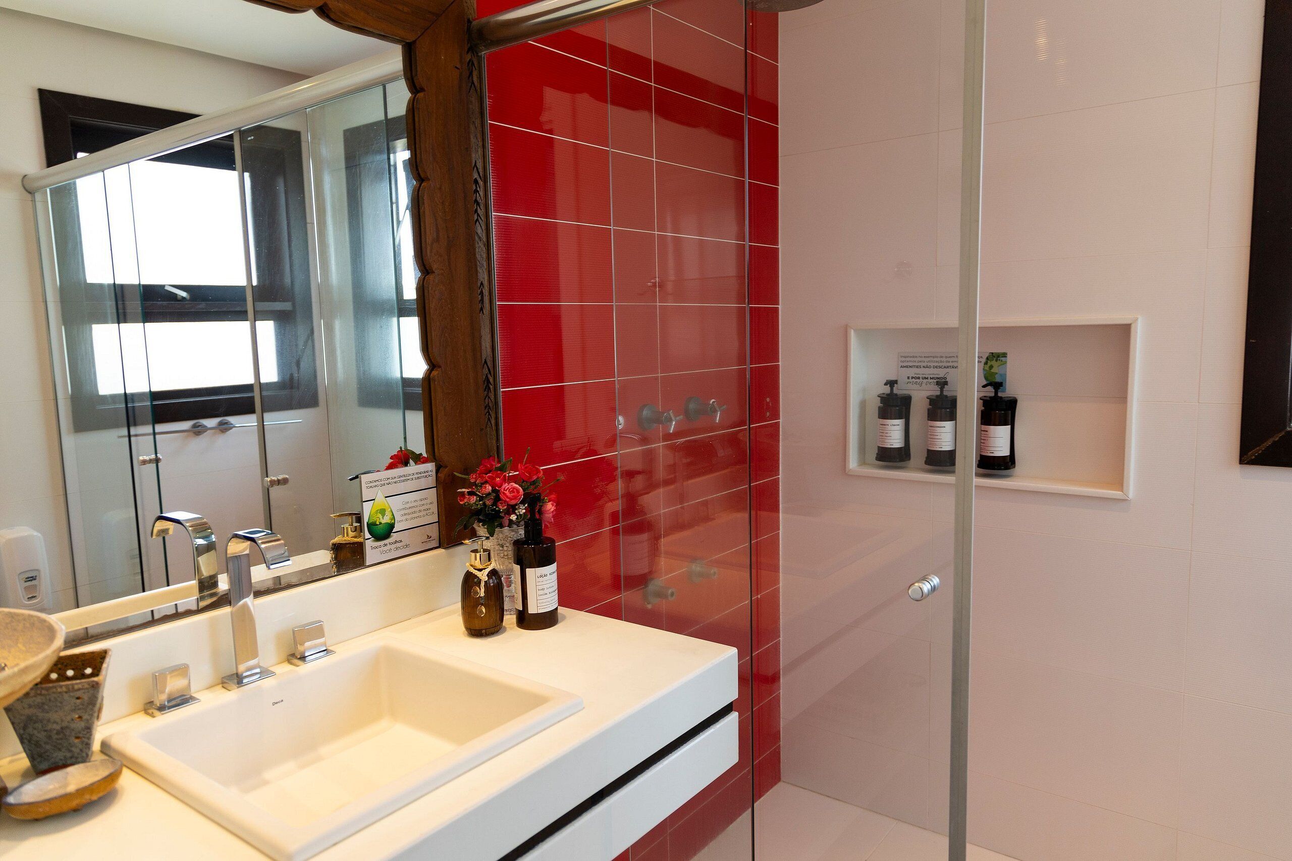Een badkamer met een witte wastafel, een douchecabine van glas en een rode betegelde wand.