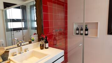Een badkamer met een witte wastafel, een douchecabine van glas en een rode betegelde wand.