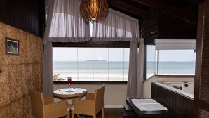 A room with a view of the ocean, a table with chairs, a small bed, and a wooden wall.
