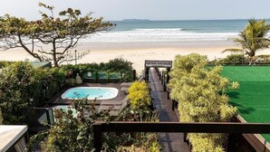 A pool area with a view of the beach, a sign reading 'República das Galinhas,' and a wooden deck.