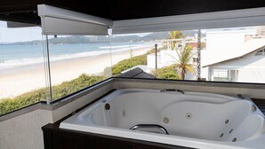 A bathroom with a large bathtub, a window overlooking a beach, and a view of the ocean.