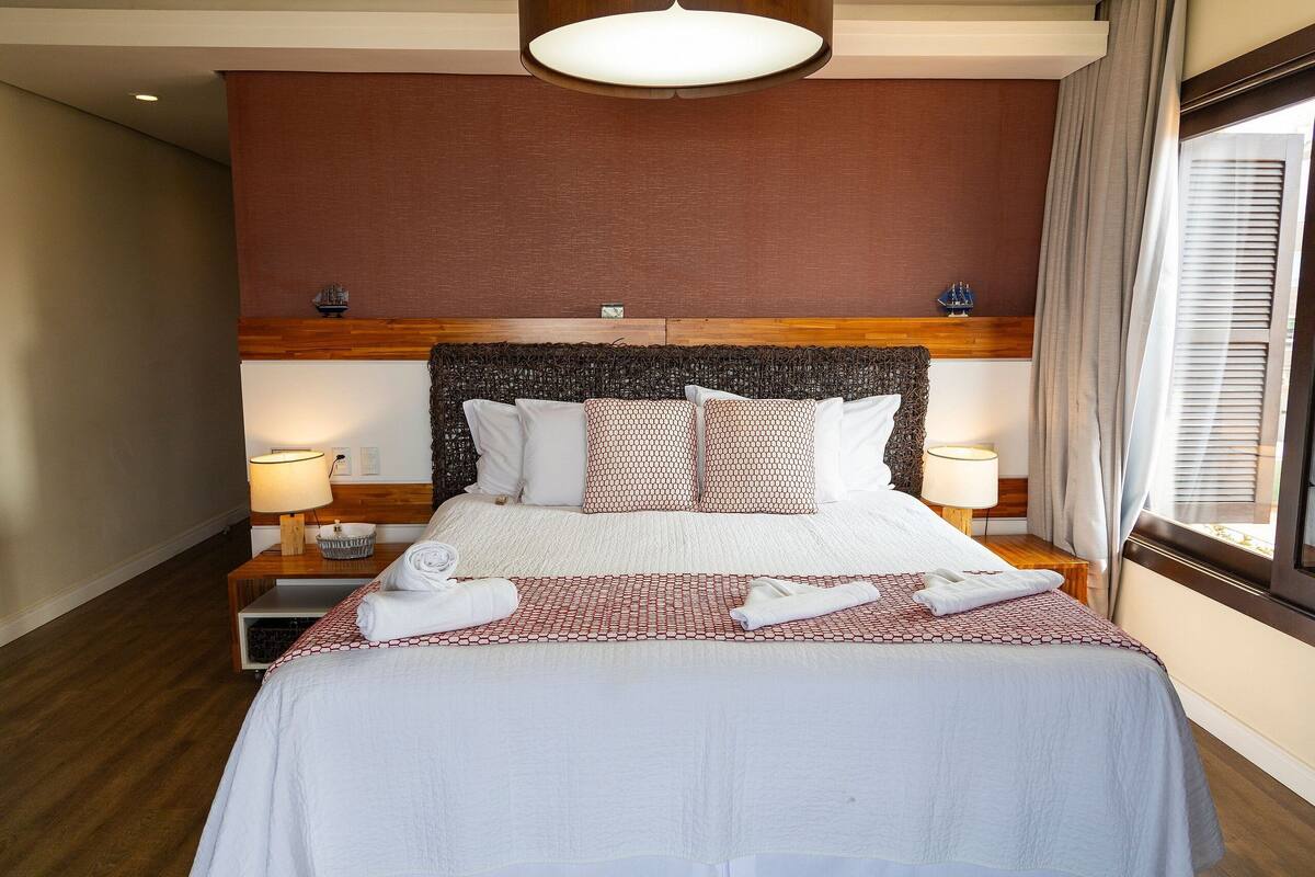 Habitación de hotel con una cama grande, dos mesitas de noche, cabecera y una ventana con cortinas.