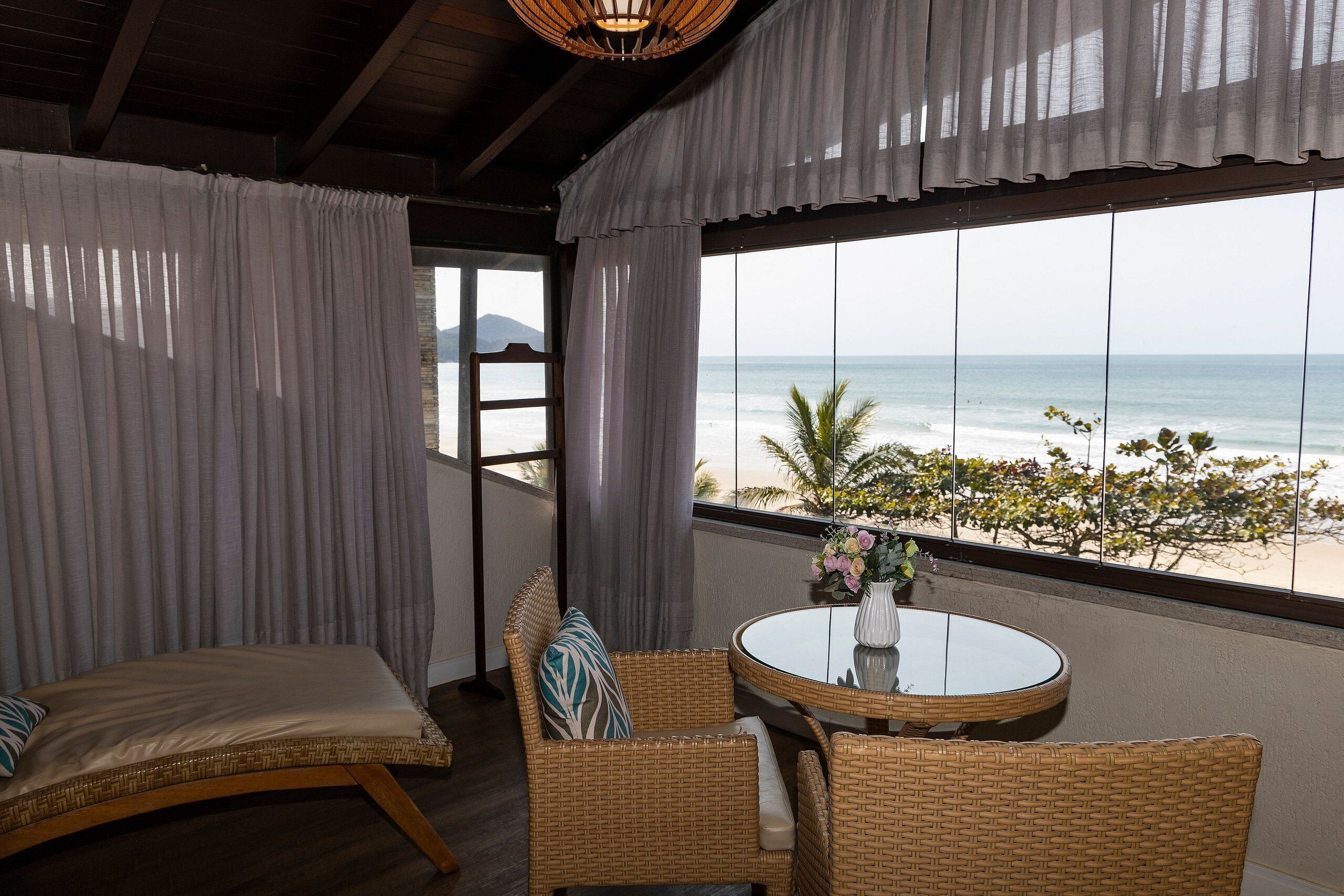 A balcony with wicker furniture, a glass table, and a view of the ocean.