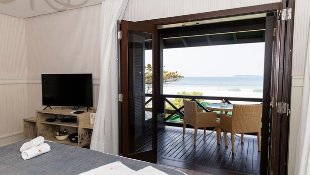 A hotel room with a bed, a TV, a balcony with a table and chairs, and a view of the ocean.