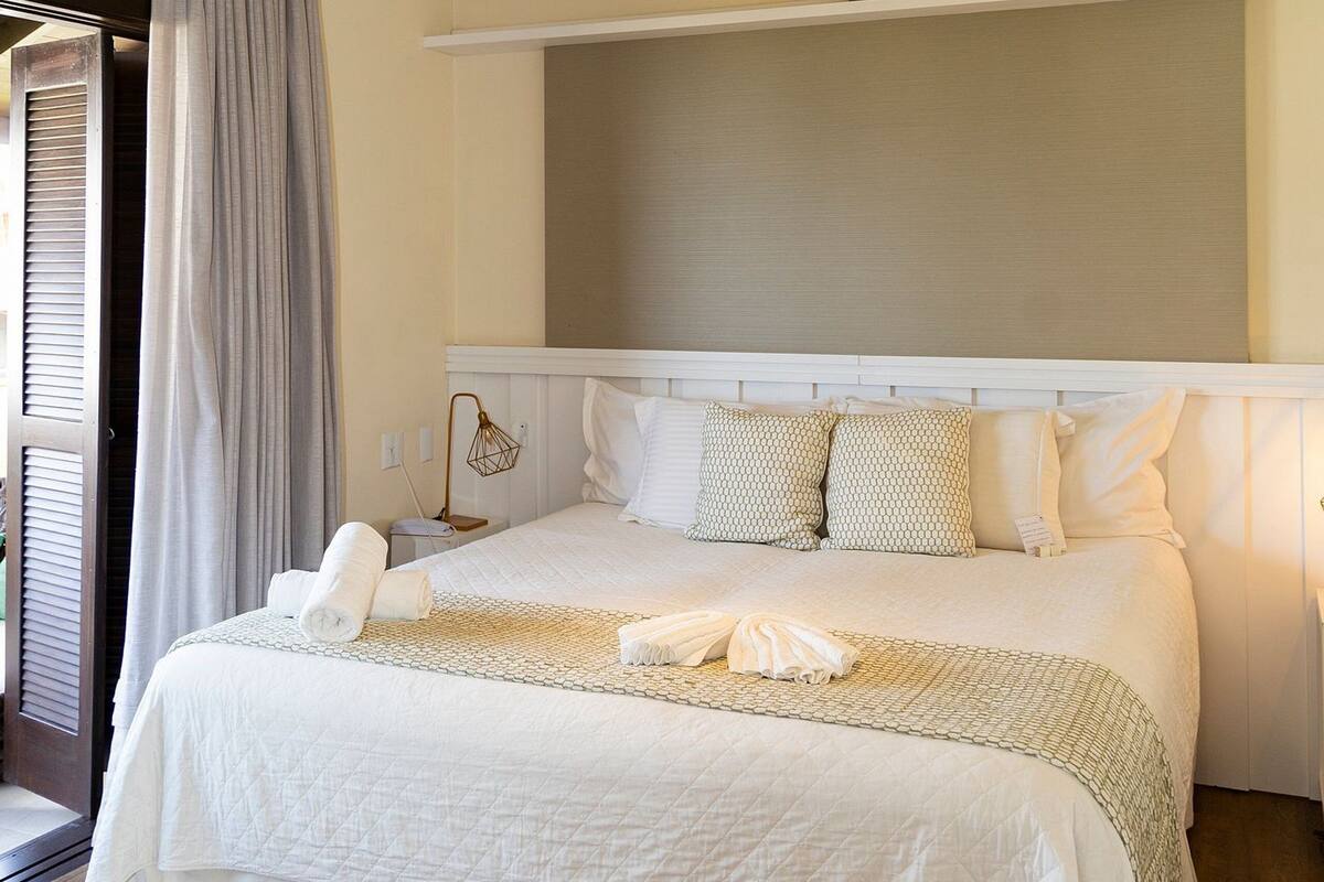 Una cama bien hecha con edredón blanco, una lámpara de noche y un cabecero.
