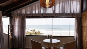 A room with a view of the ocean, a wicker table with chairs, a bed, and a hanging light fixture.