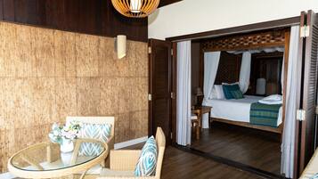 Una habitación con una cama, una mesita de vidrio, muebles de mimbre y techo de madera.