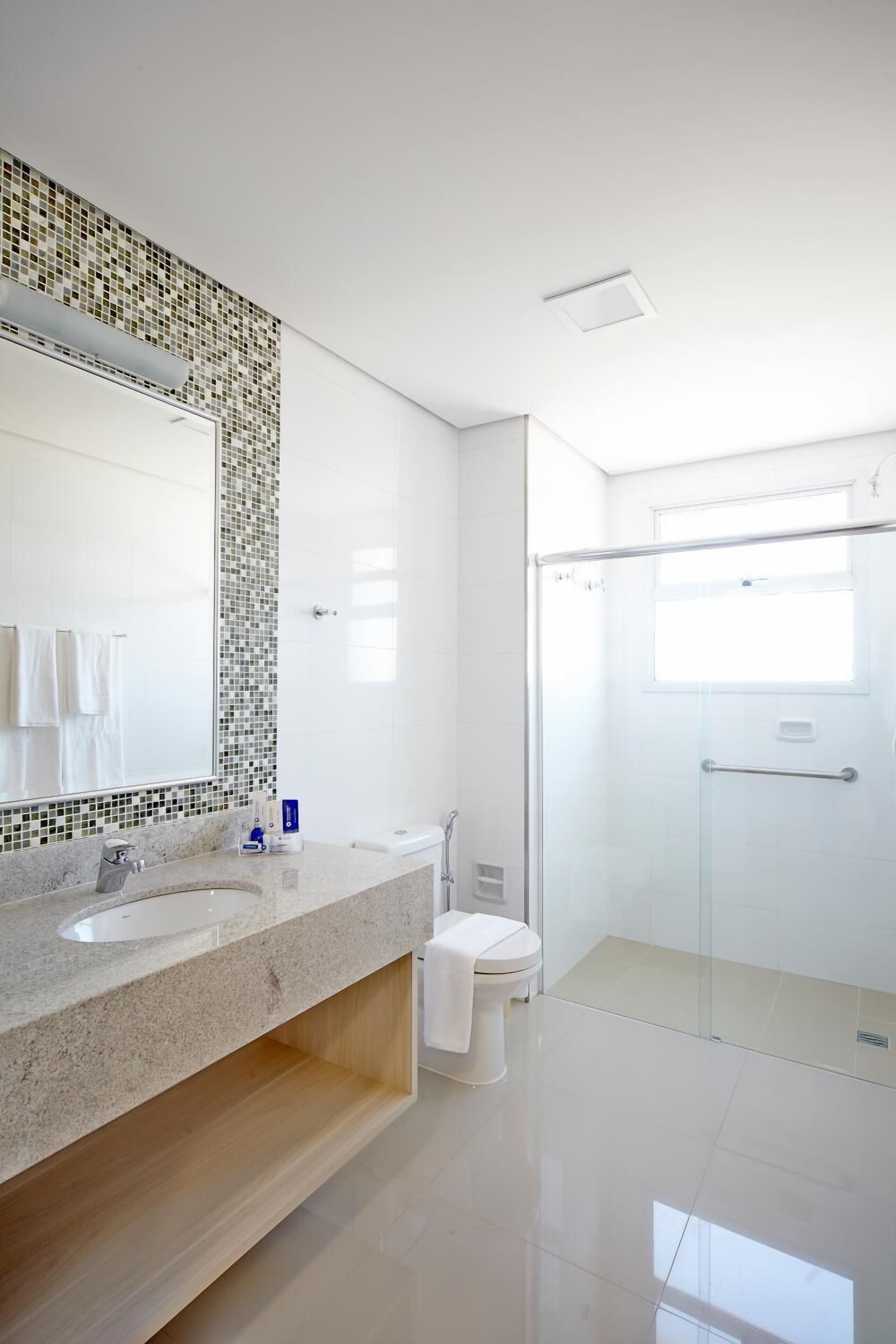 Un baño moderno con cabina de ducha de vidrio, lavabo blanco y salpicadero de azulejos.