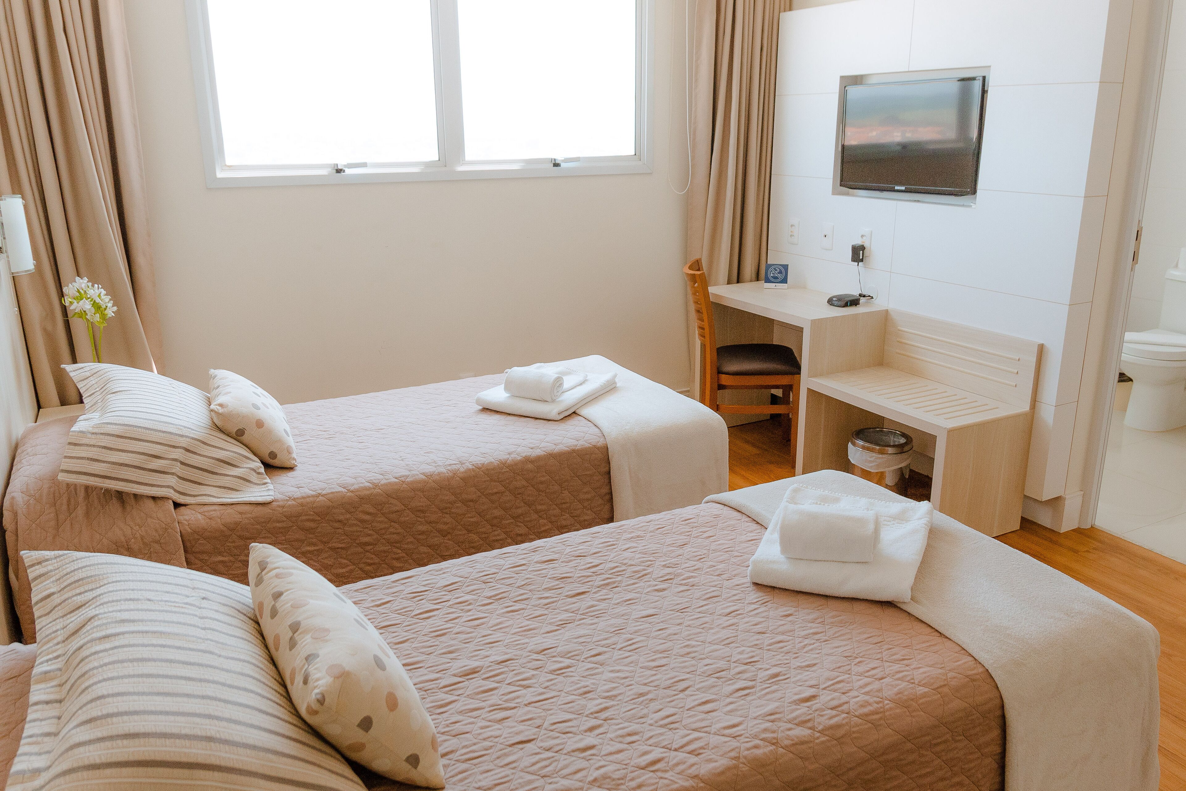 Una habitación de hotel con dos camas, un escritorio, un televisor y una ventana.