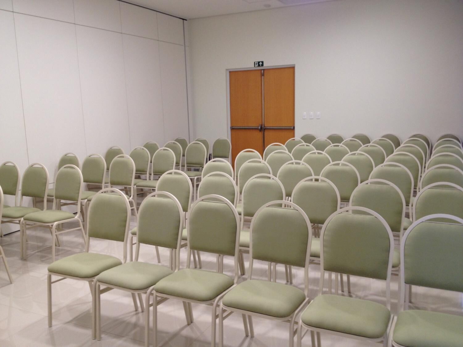 A conference room with rows of green chairs and a wooden door.
