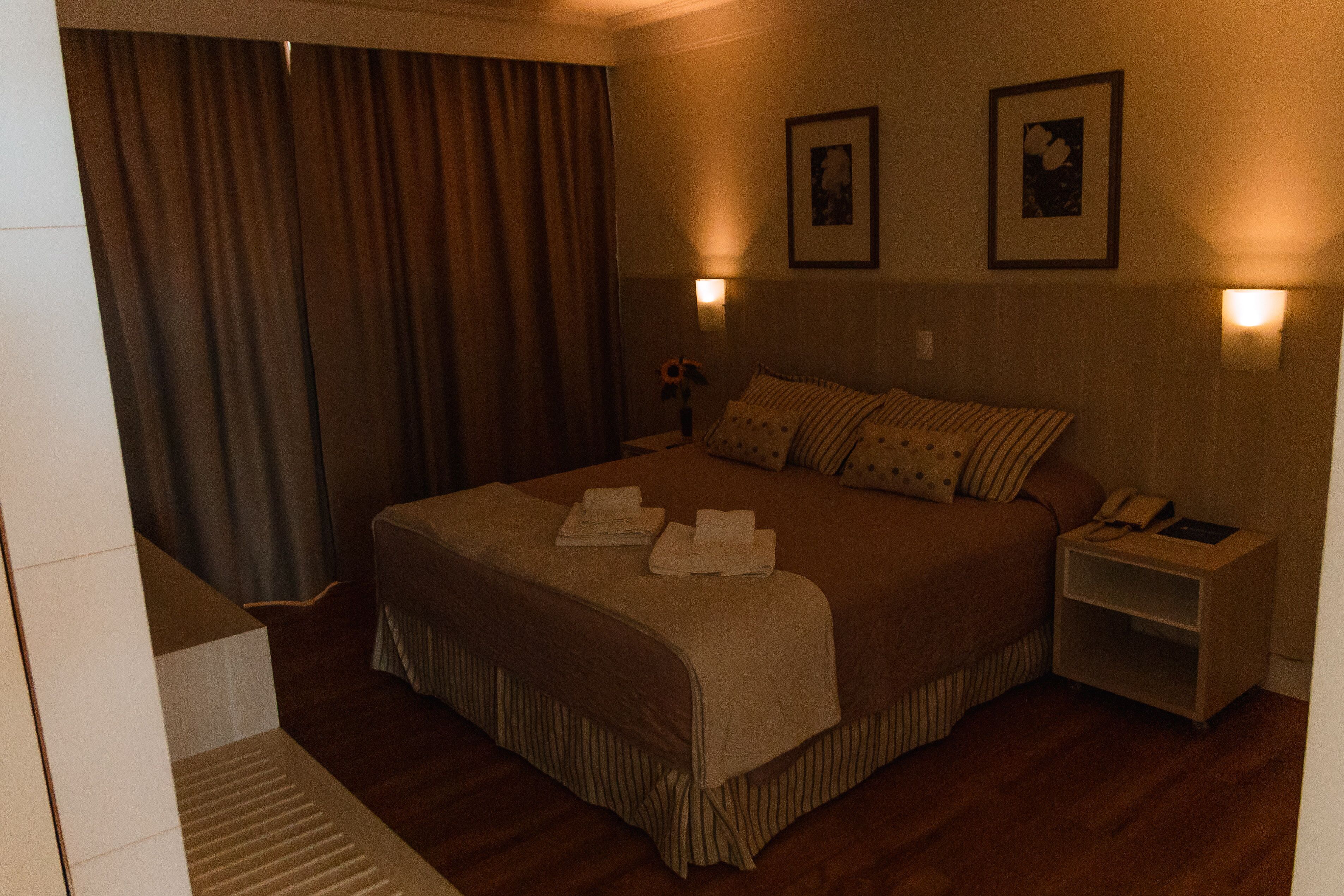 Habitación de hotel con una cama grande, dos lámparas de noche, una mesita de noche y una ventana con cortinas.