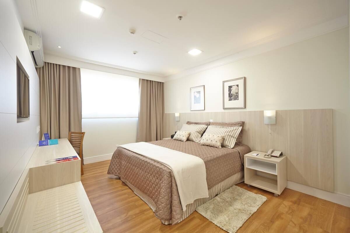 A modern hotel room with a large bed, bedside tables, a desk, and a window with curtains.