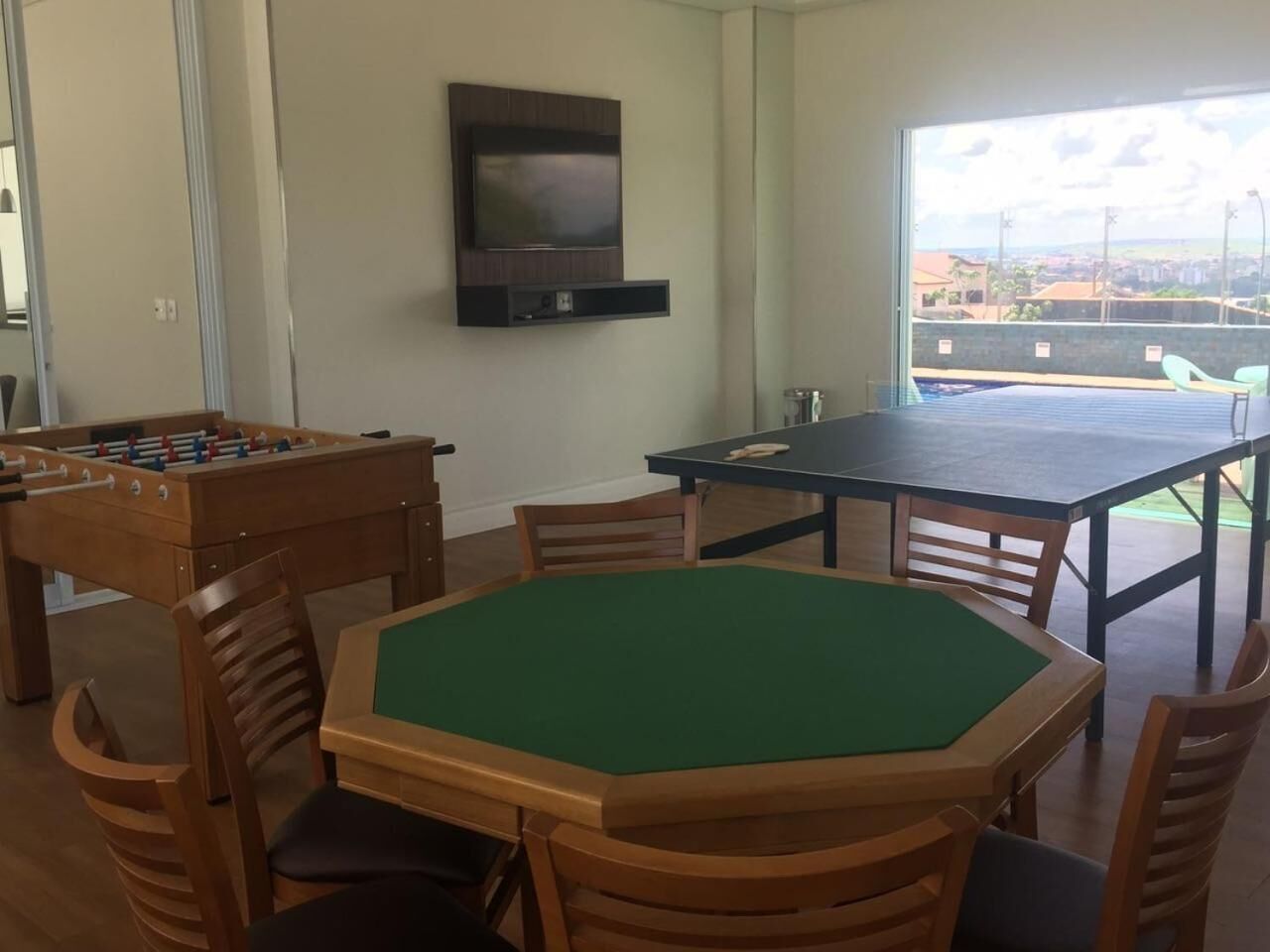 Um quarto com mesa de pebolim, mesa de bilhar e uma televisão na parede.