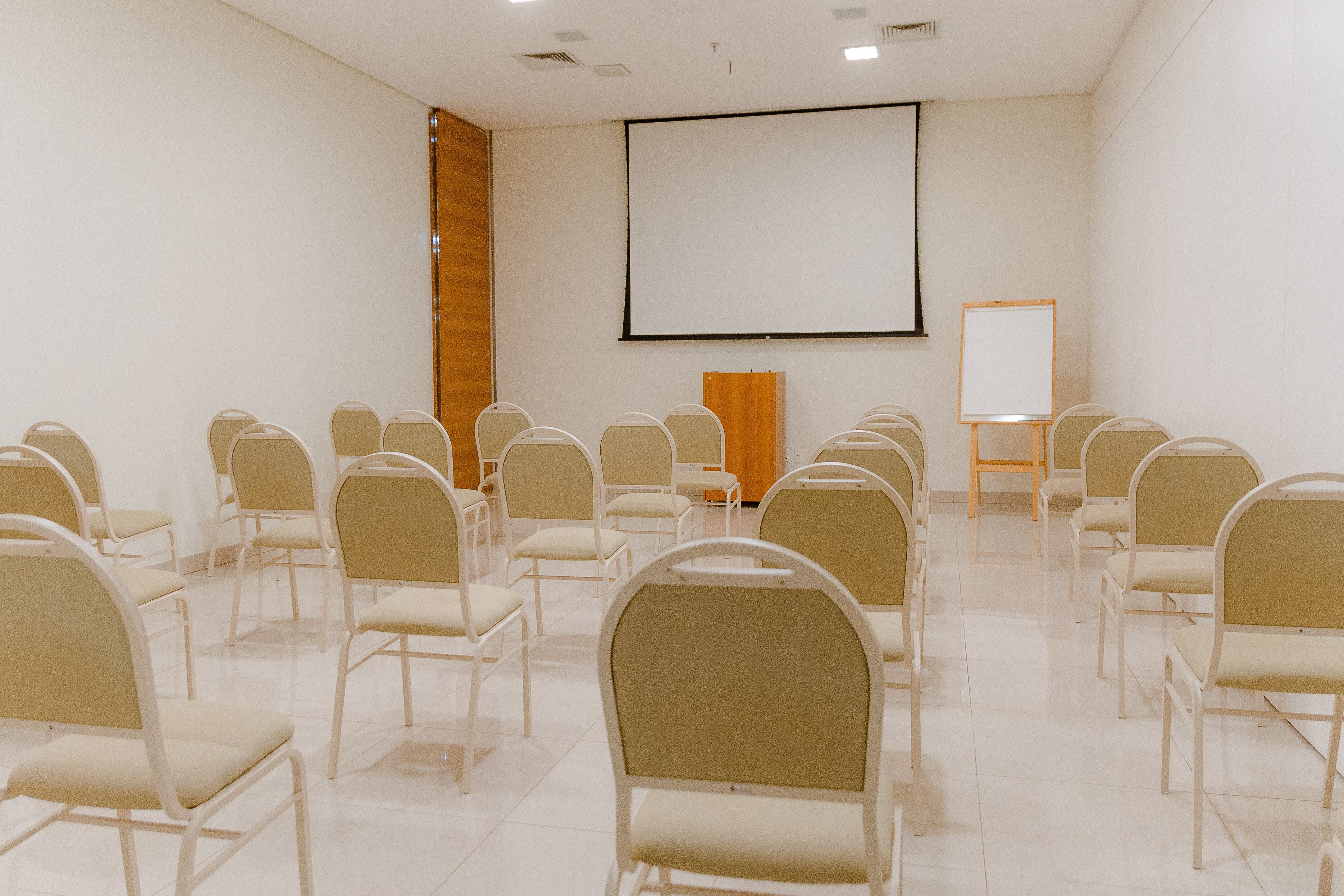 A conference room with rows of chairs, a projector screen, and a whiteboard.