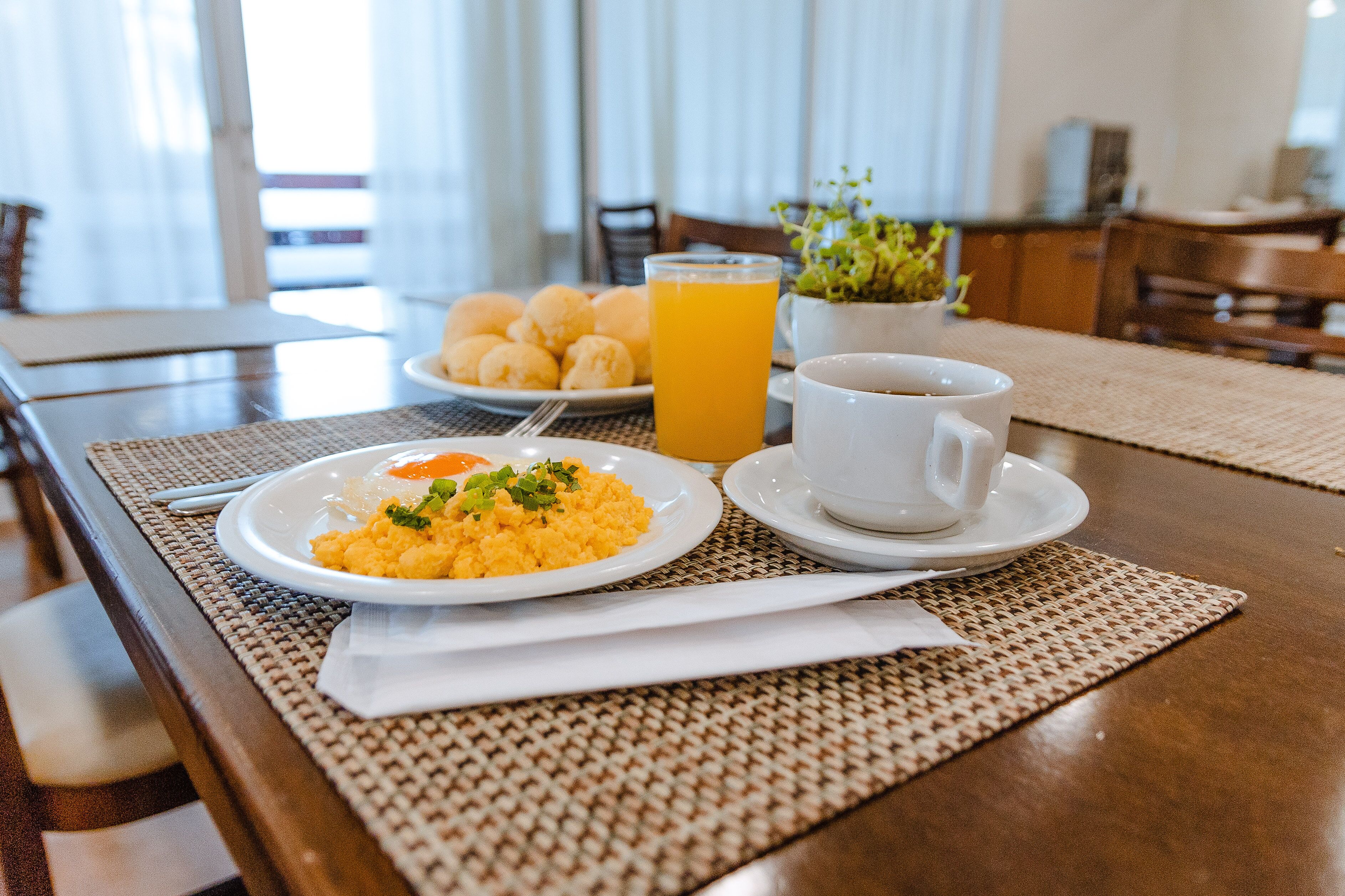 Desayuno con huevos revueltos, un vaso de zumo de naranja y una taza de café sobre una mesa de madera.
